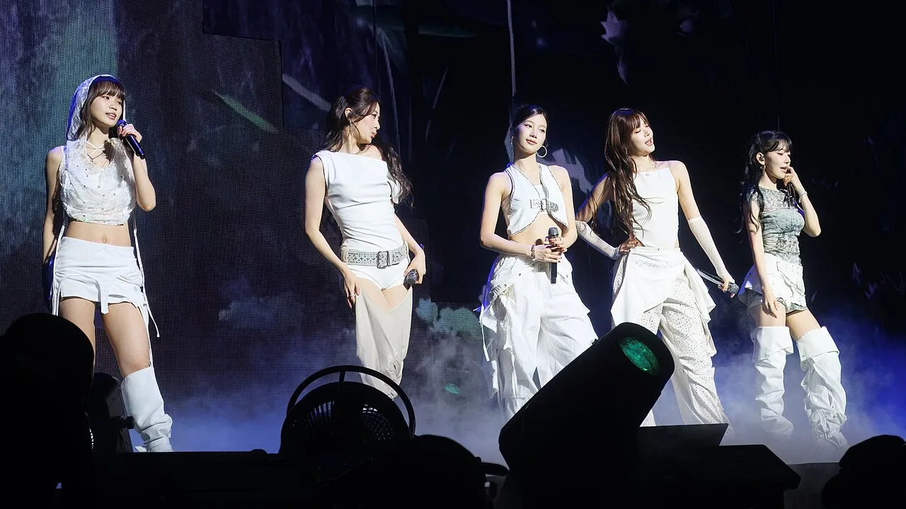 The five members of LE SSERAFIM standing in a row in white stage outfits, microphones in hand, at the EASY CRAZY HOT tour show in Seattle on 17 September 2025