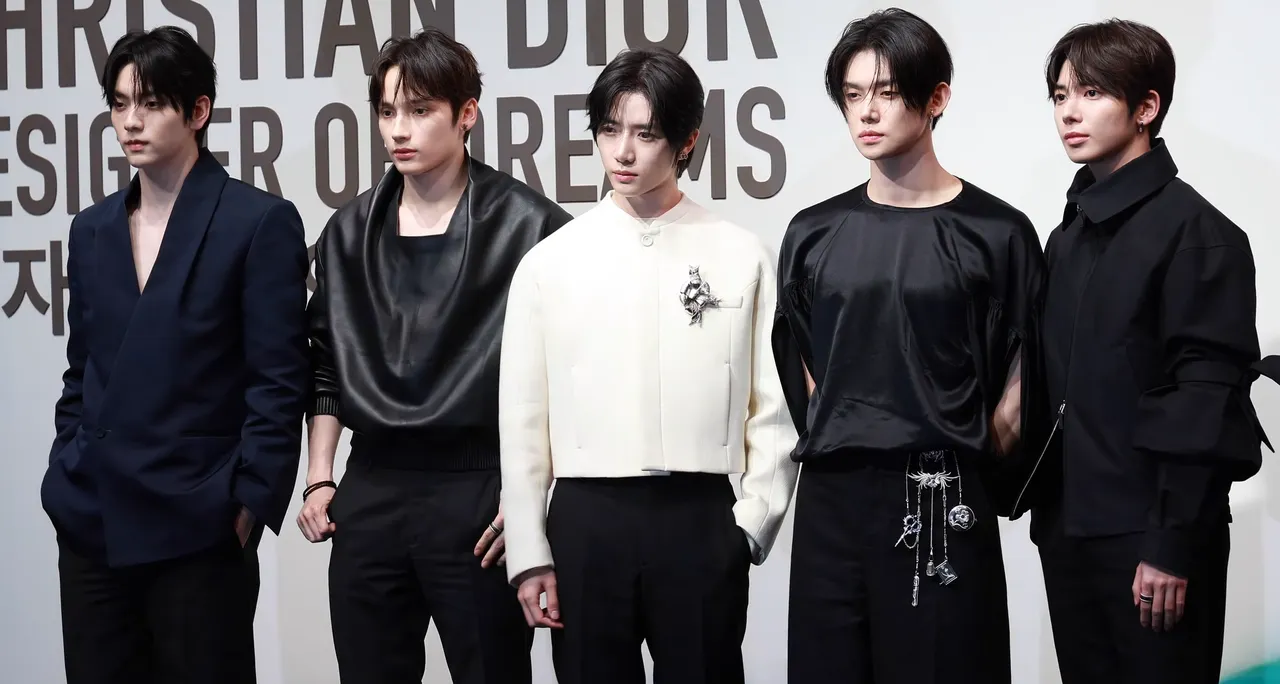 The five members of TOMORROW X TOGETHER standing side by side on 18 April 2025 in front of a Dior exhibition photo wall lettered 'CHRISTIAN DIOR DESIGNER OF DREAMS'.